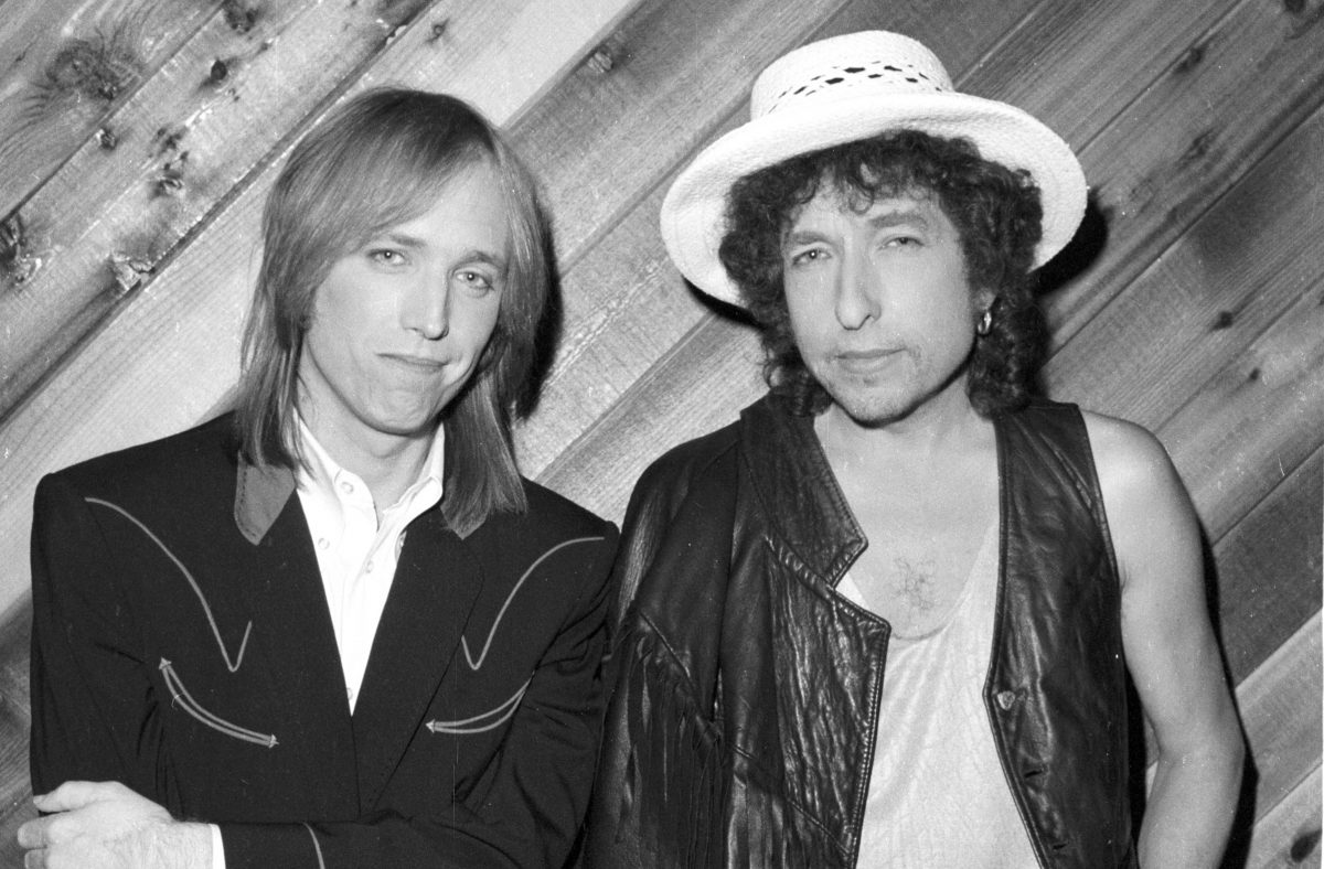 Une photo en noir et blanc de Tom Petty et Bob Dylan appuyés contre un mur lambrissé.