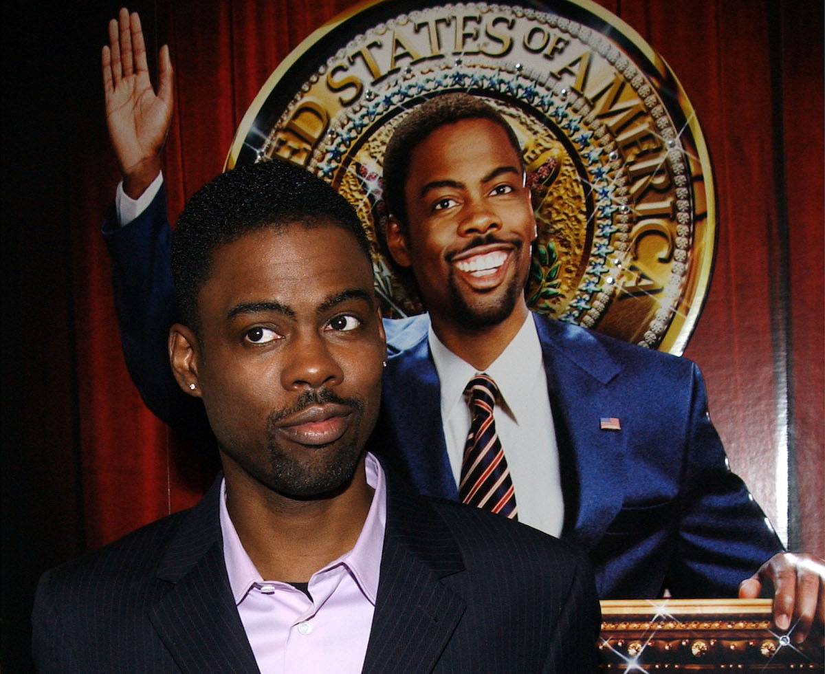 Chris Rock porte un costume et pose devant une affiche pour 'Head of State'