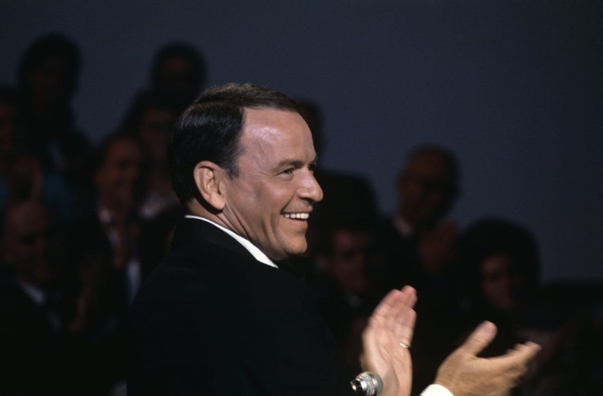 Frank Sinatra se tient près d'un micro et tape dans ses mains.