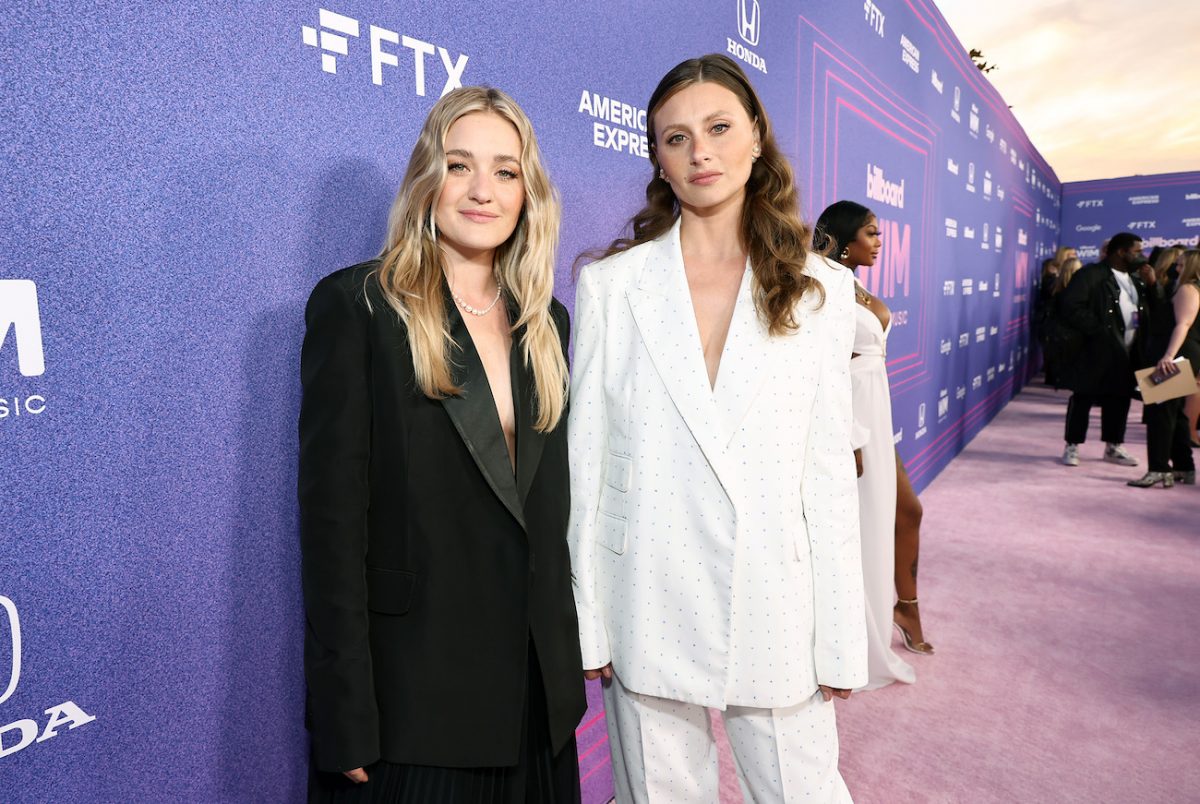 Amanda Michalka portant un costume surdimensionné noir et Aly Michalka portant un costume surdimensionné blanc, toutes deux debout devant un fond violet