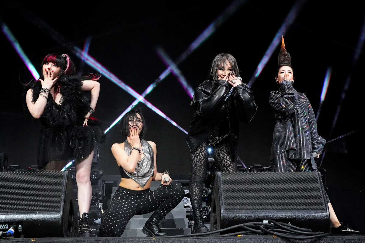 Se couvrant la bouche avec leurs mains, les quatre membres du groupe K-pop 2NE1 se produisent sur scène au Coachella Valley Music Festival à Indio, en Californie.
