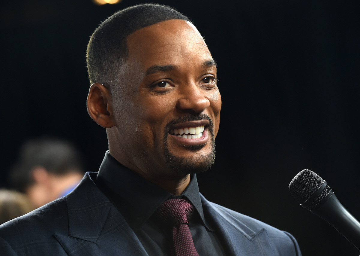 Will Smith sourit en costume devant un micro
