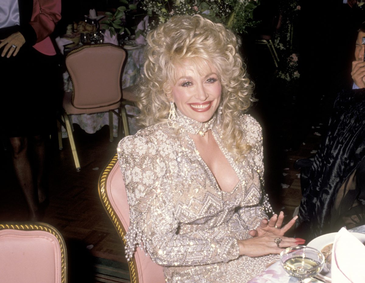 Dolly Parton porte une robe perlée blanche et est assise sur une chaise rose lors de la première de 