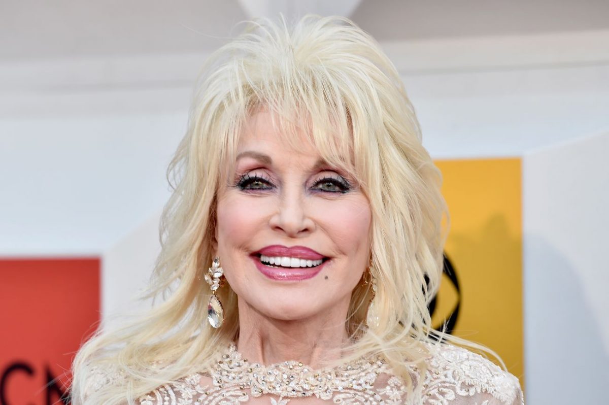 Dolly Parton porte une robe en dentelle blanche et des boucles d'oreilles en cristal.