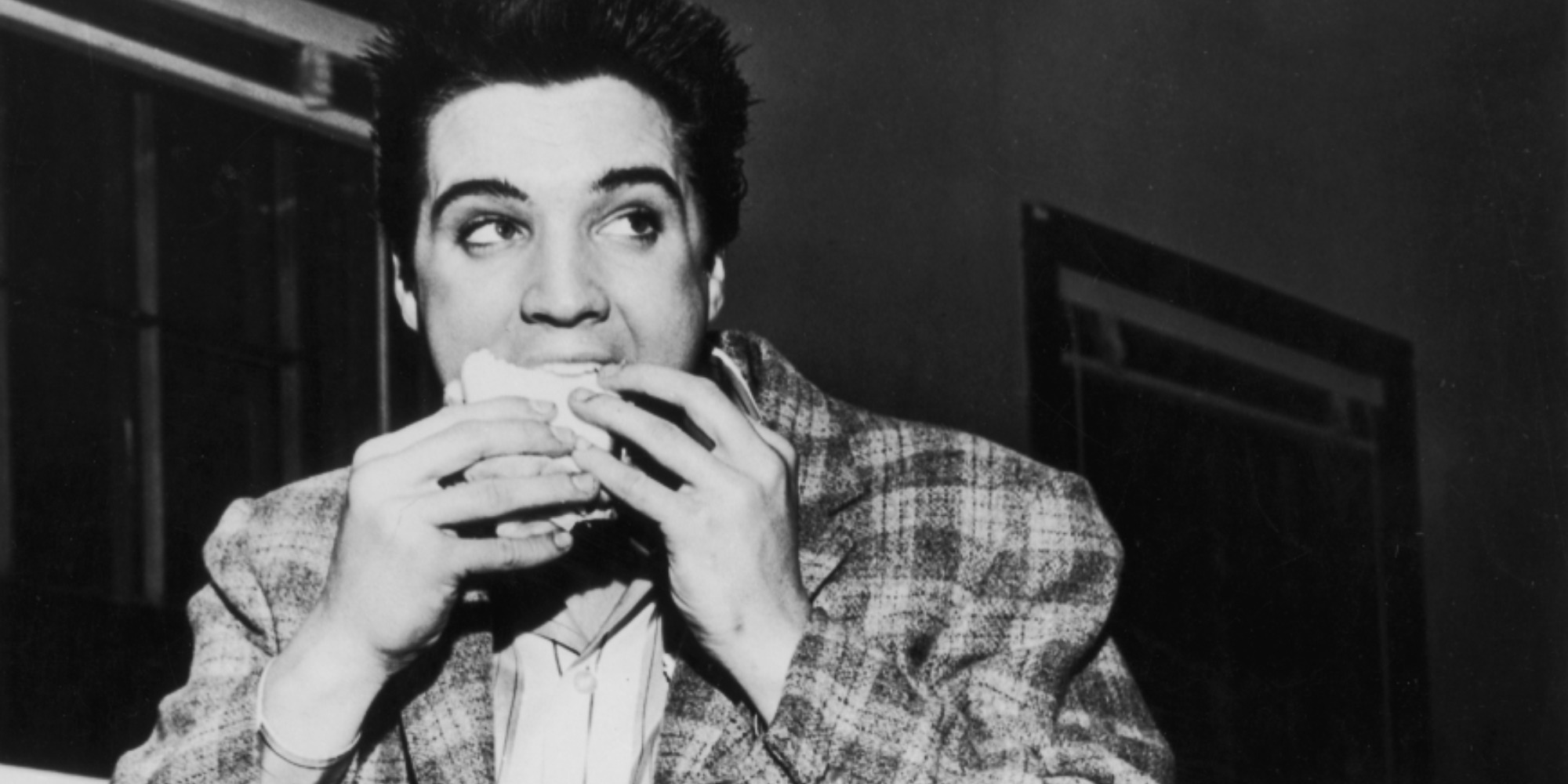 Elvis Presley déguste un sandwich sur une photo en noir et blanc.