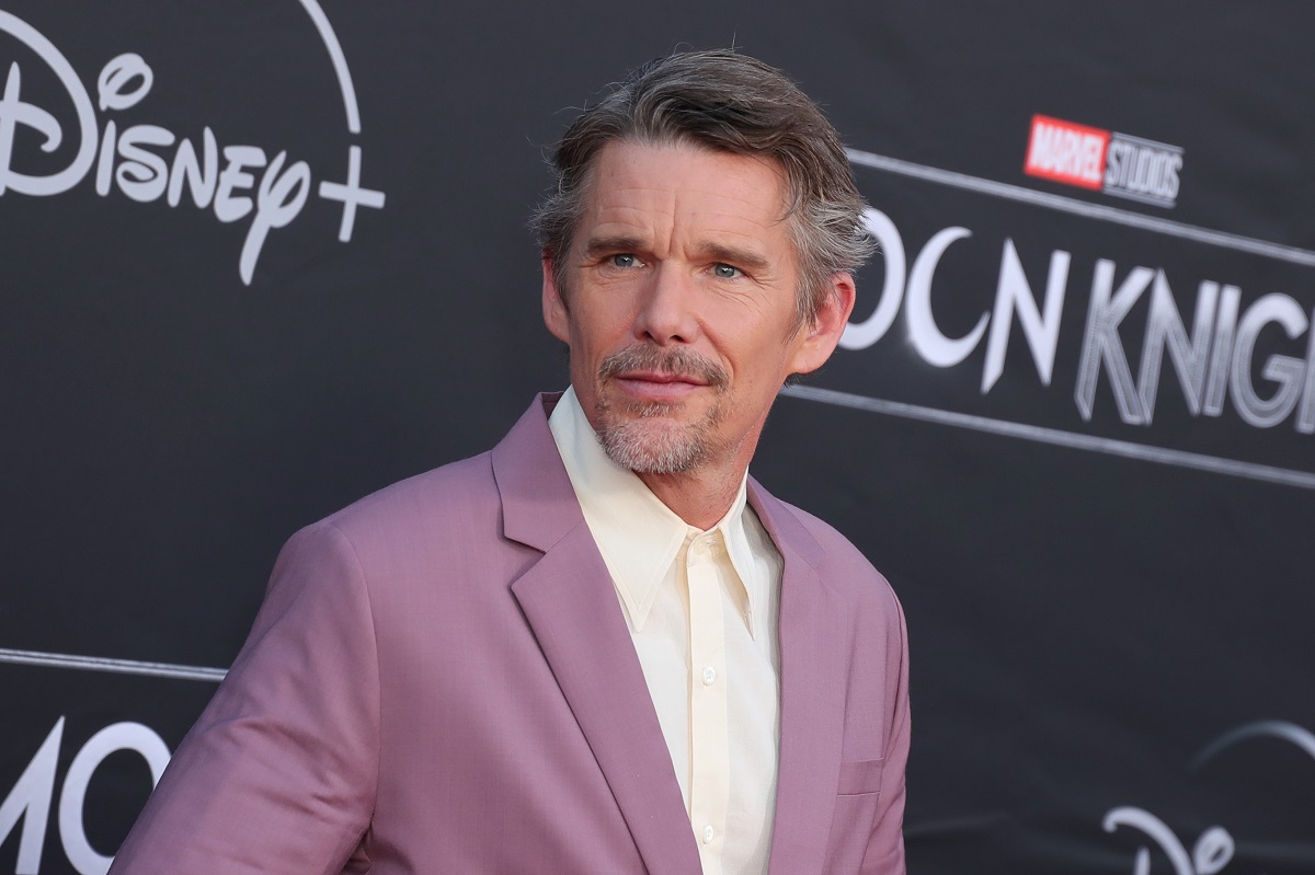 Ethan Hawke souriant en portant un costume violet.
