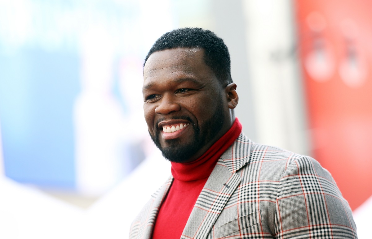 50 Cent sourit en portant un col roulé rouge et un costume.