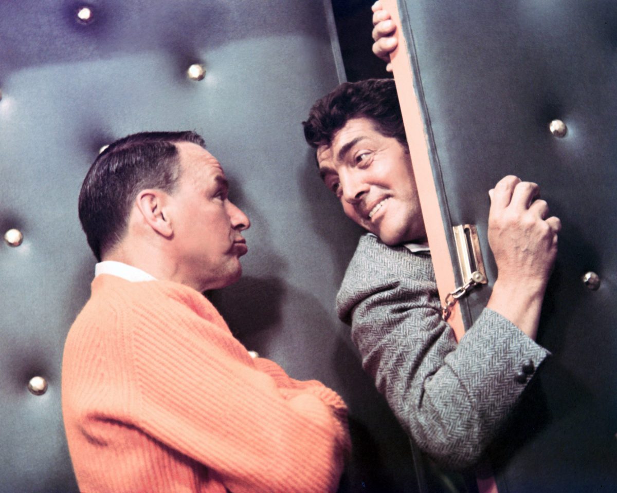 Dean Martin passe la tête et l'épaule par une porte verrouillée.  Frank Sinatra se tient les bras croisés et fait face à Martin.