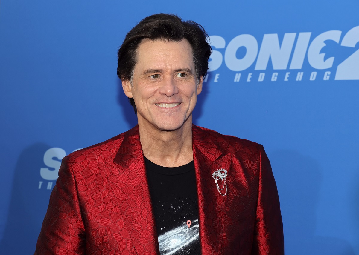 Jim Carrey souriant tout en portant une veste rouge.