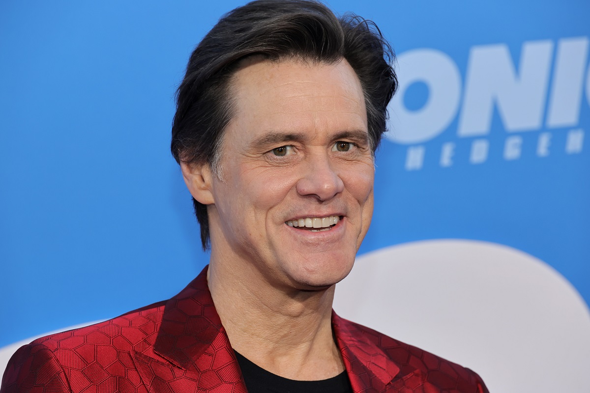 Jim Carrey souriant tout en portant une veste rouge.