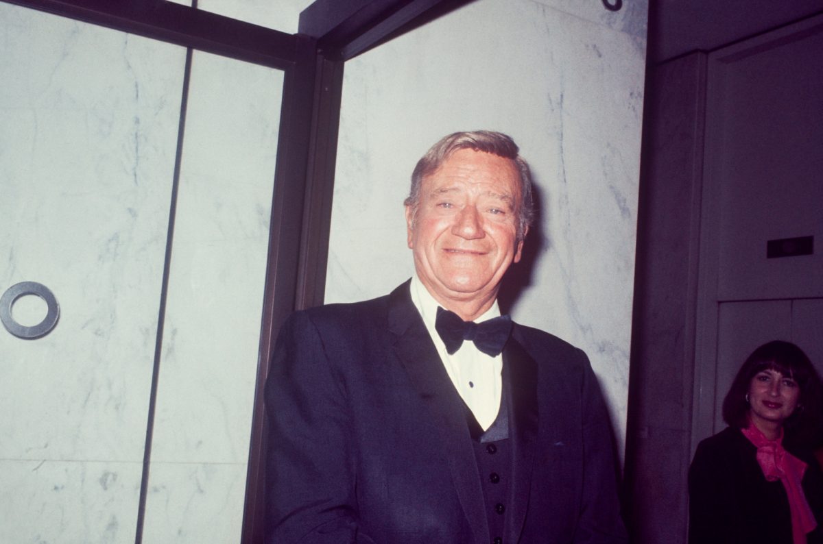 Le présentateur des Oscars 1973 John Wayne souriant vêtu d'un smoking