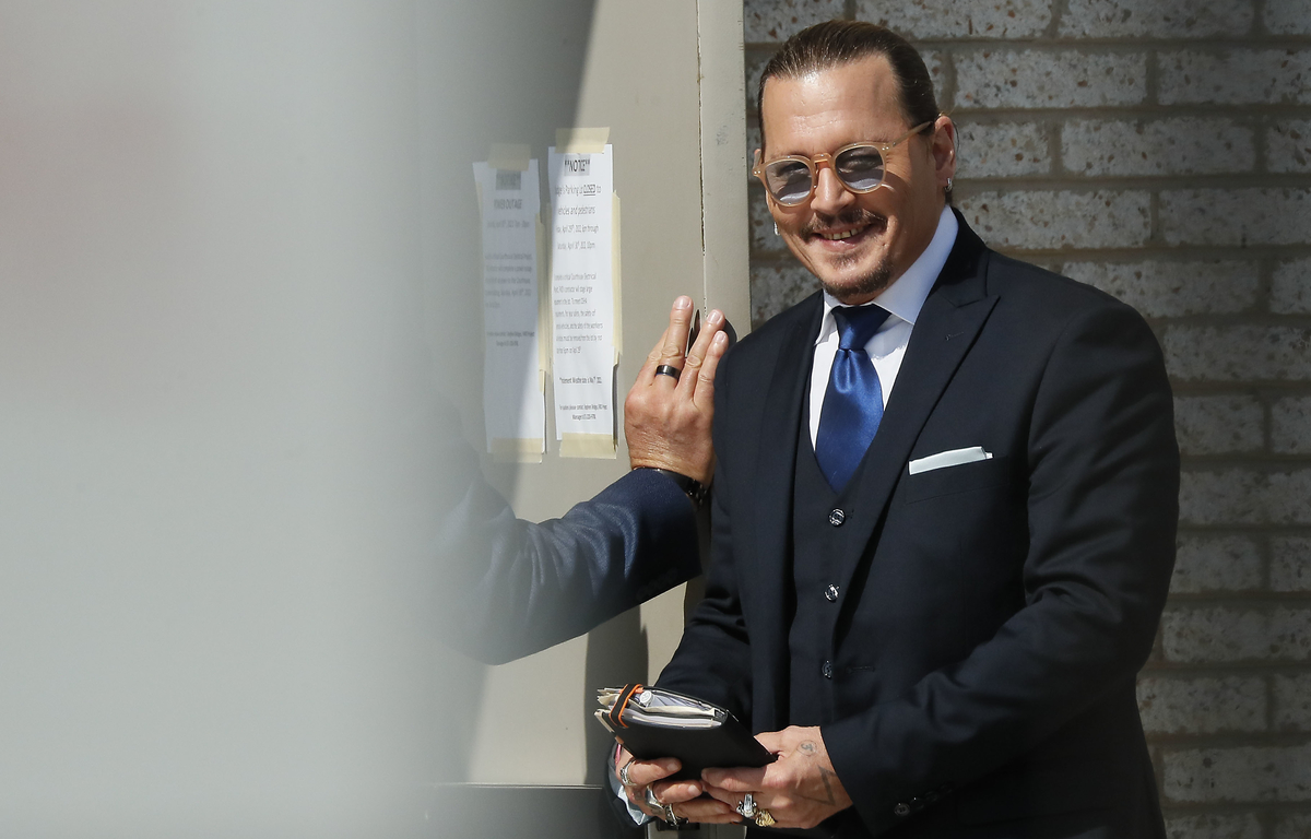 Johnny Depp se tient à l'extérieur de la salle d'audience en costume tout en souriant.