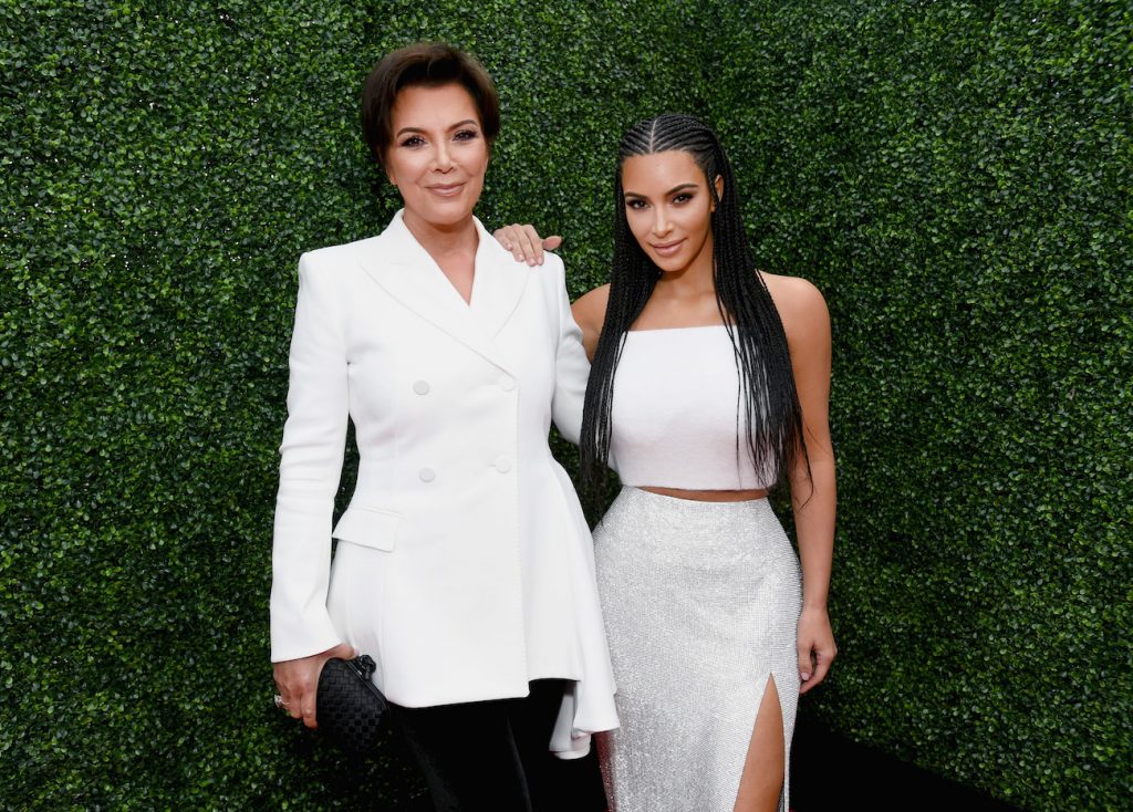 Kris Jenner et Kim Kardashian debout côte à côte dans des tenues blanches et devant un fond vert foncé