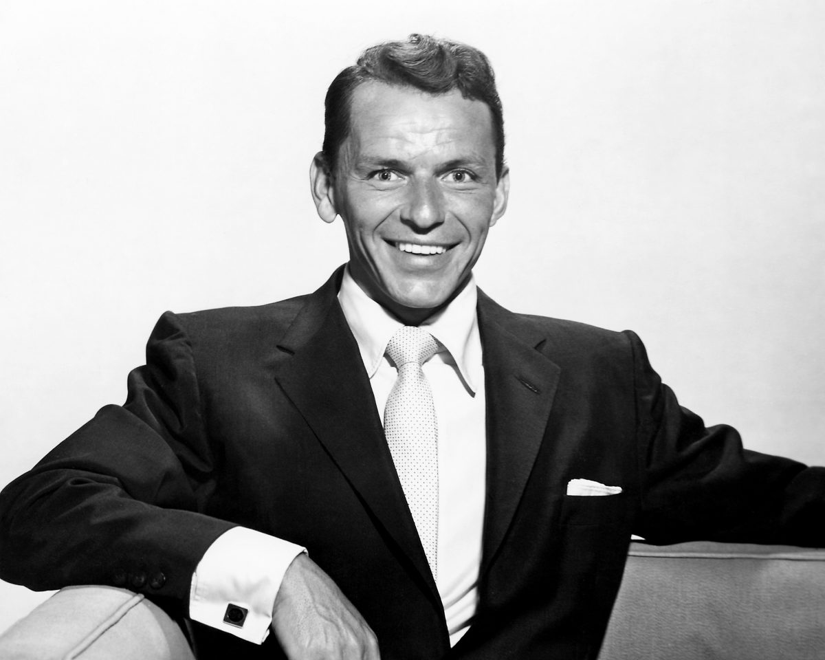 Une photo en noir et blanc de Frank Sinatra assis et vêtu d'un costume.