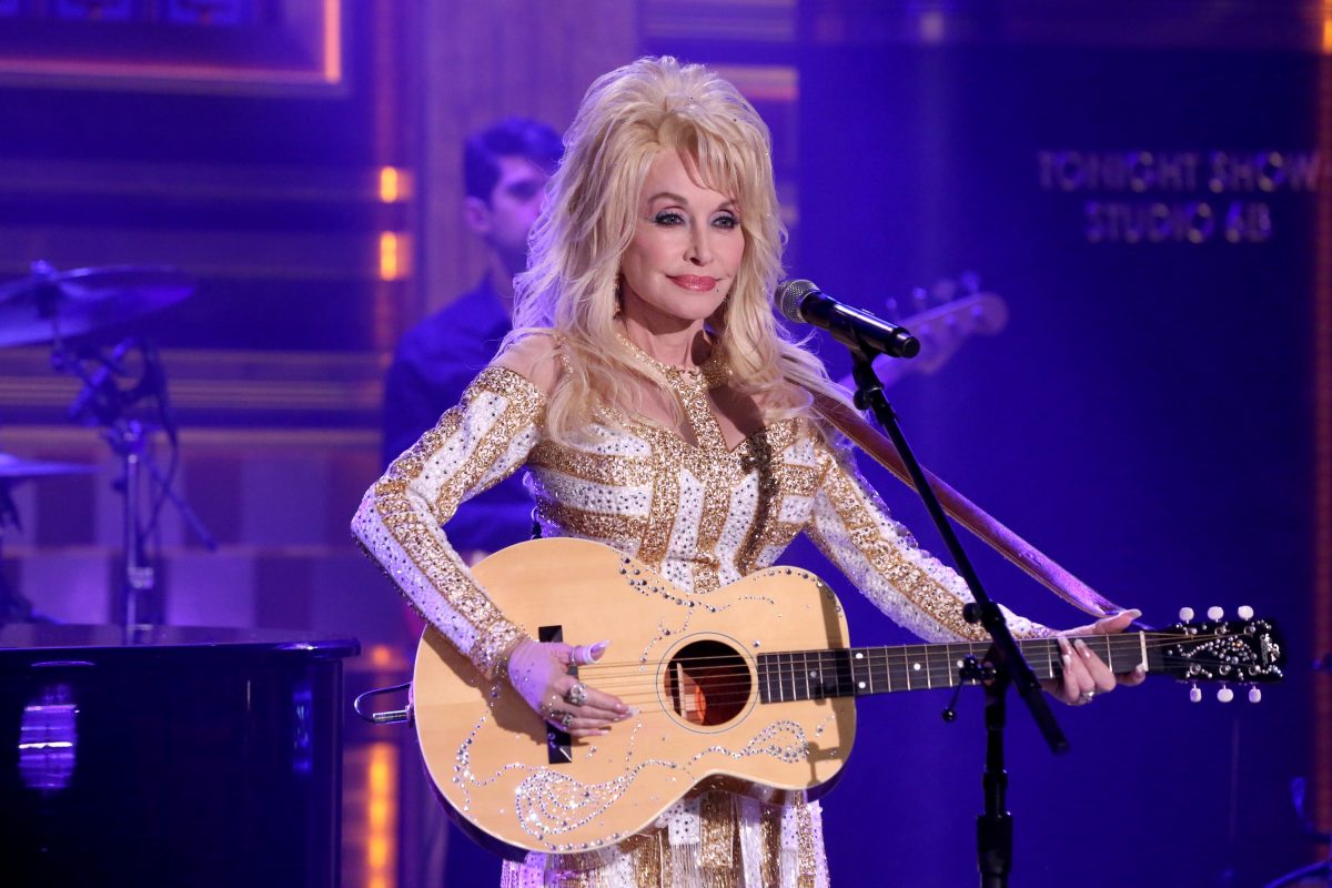 Dolly Parton porte de l'or et du blanc en jouant de la guitare. 