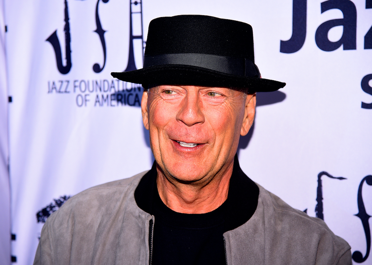 Bruce Willis porte un chapeau noir et sourit