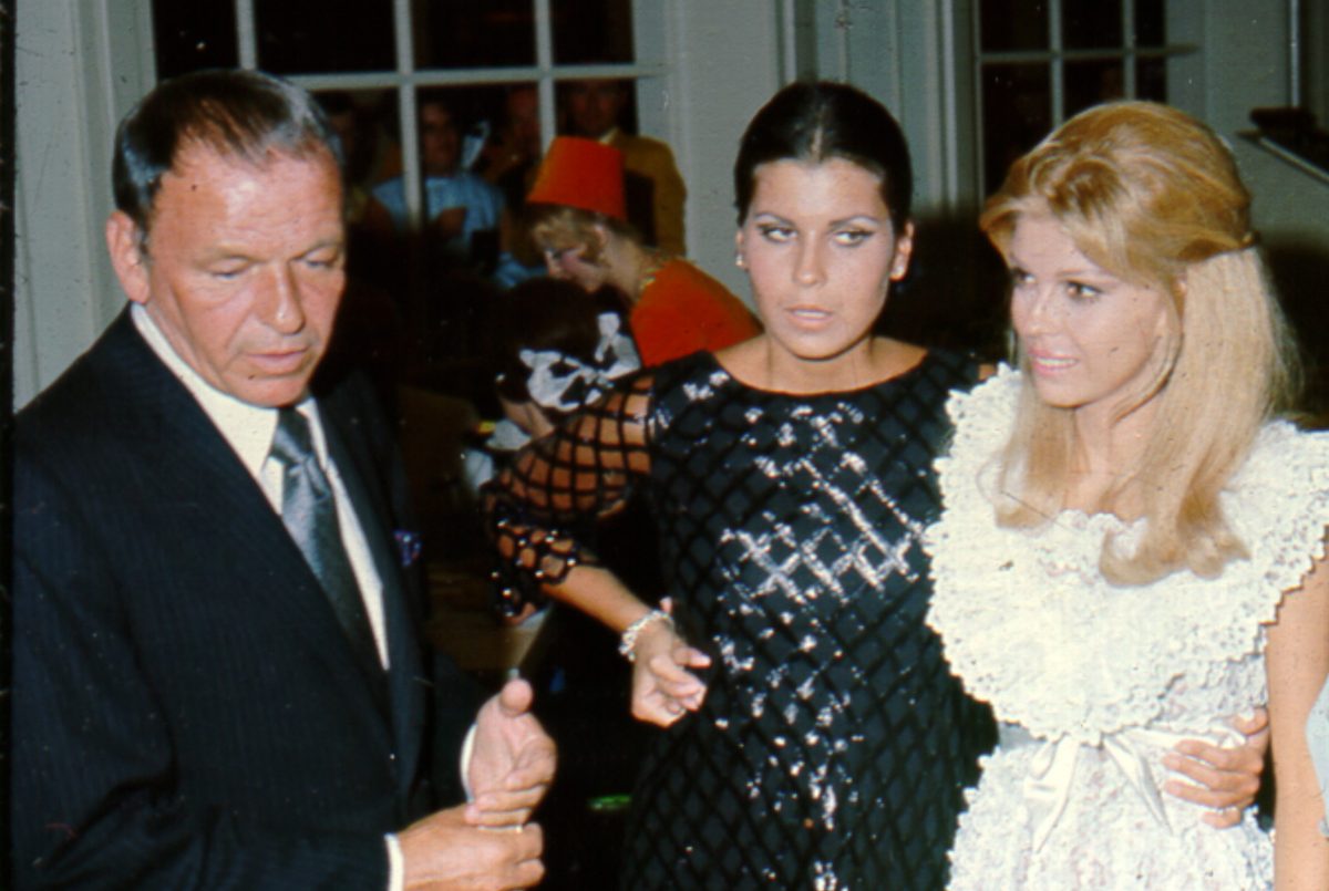 Frank Sinatra porte un costume, Tina Sinatra porte une robe noire et Nancy Sinatra porte une robe blanche lors d'une fête.
