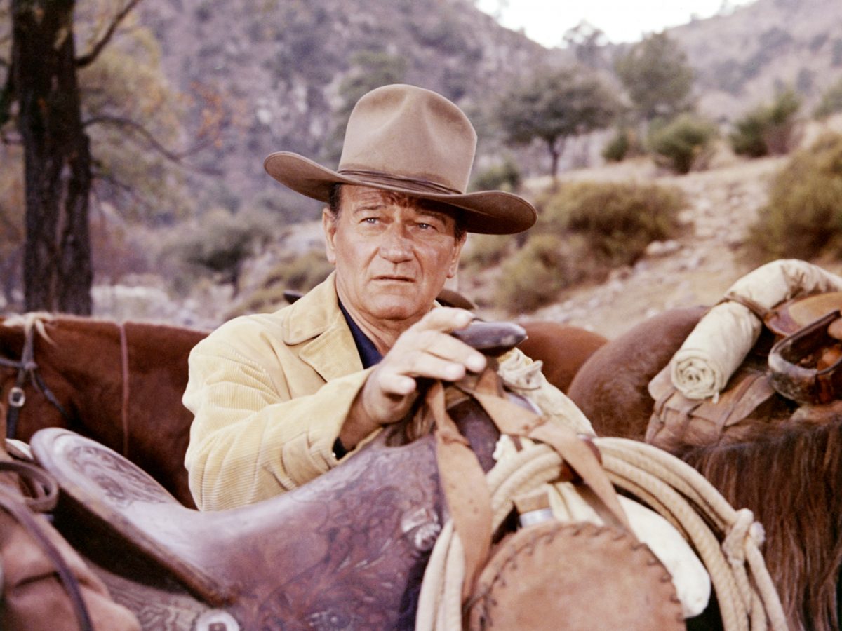 'The Sons of Katie Elder' John Wayne dans le rôle de John portant un chapeau de cow-boy avec une main sur la selle avec les collines en arrière-plan