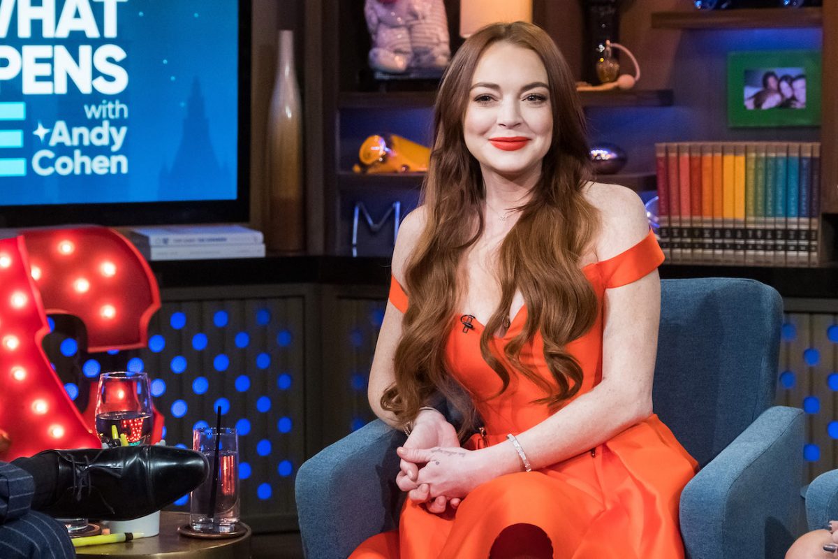 Lindsay Lohan portant une robe rouge à épaules dénudées et assise sur une chaise bleue