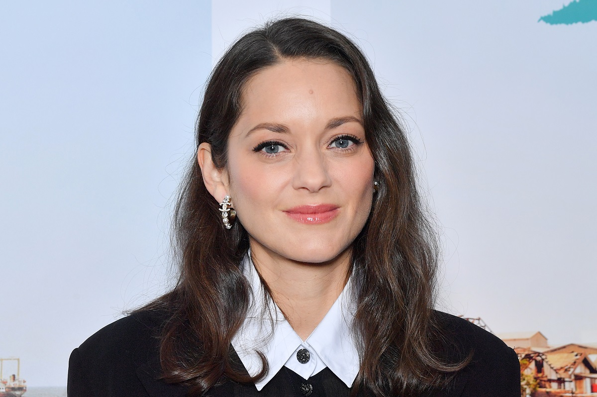 Marion Cotillard souriant en portant un pull noir.