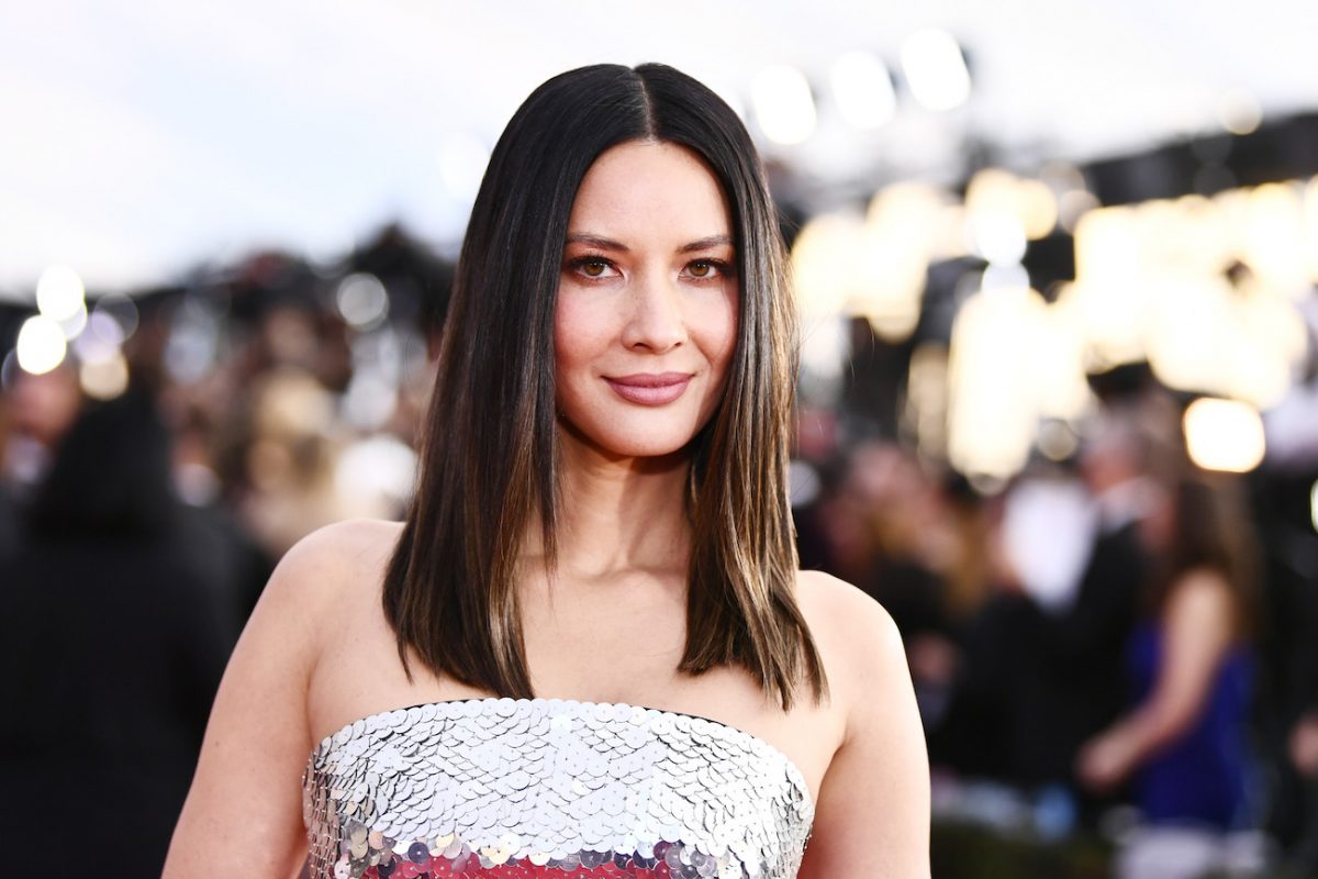 Olivia Munn portant une tenue blanche sans bretelles et souriant à la caméra