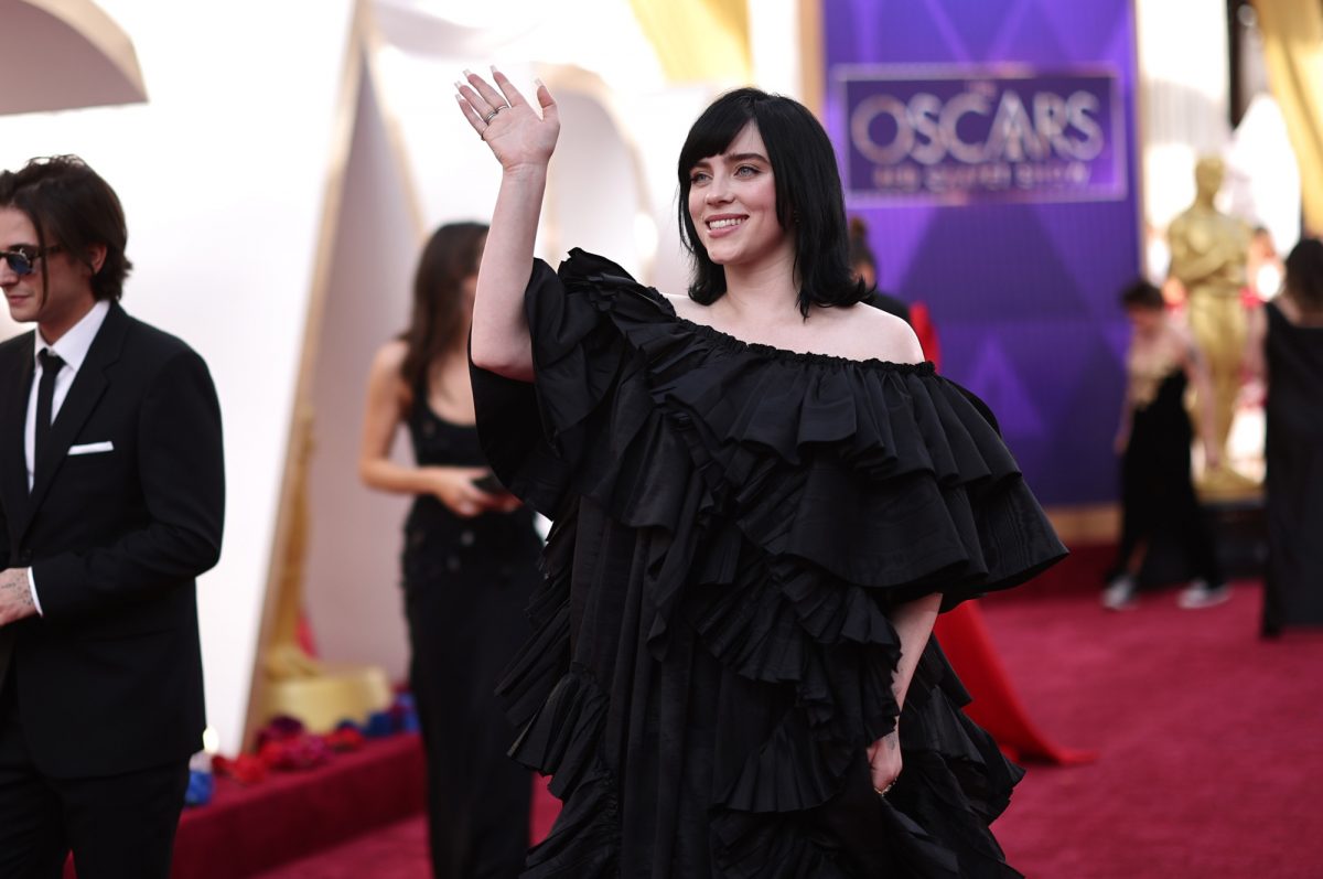 La chanteuse Billie Eilish, qui a chanté la chanson 'No Time to Die' dans le film de Daniel Craig portant une robe noire agitant la main sur le tapis rouge des Oscars 2022