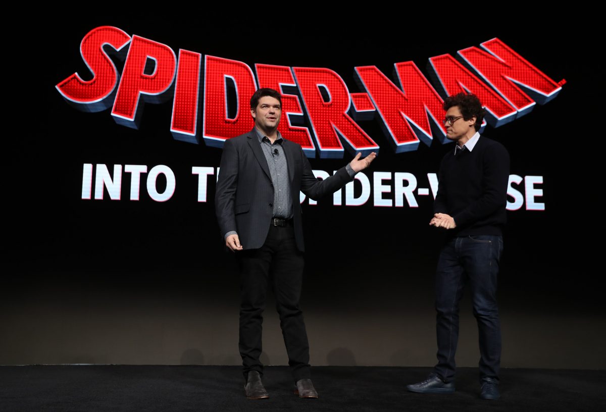 «Spider-Man: Across the Spider-Verse», qui est retardé, les écrivains Christopher Miller et Phil Lord parlent sur scène.  Miller porte un costume gris foncé sur une chemise boutonnée gris clair et un pantalon noir.  Lord porte un pull noir sur une chemise à col blanc et un jean.