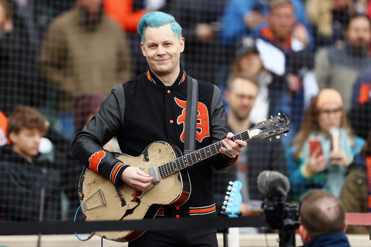 Jack White tenant une guitare et souriant à un match de sport