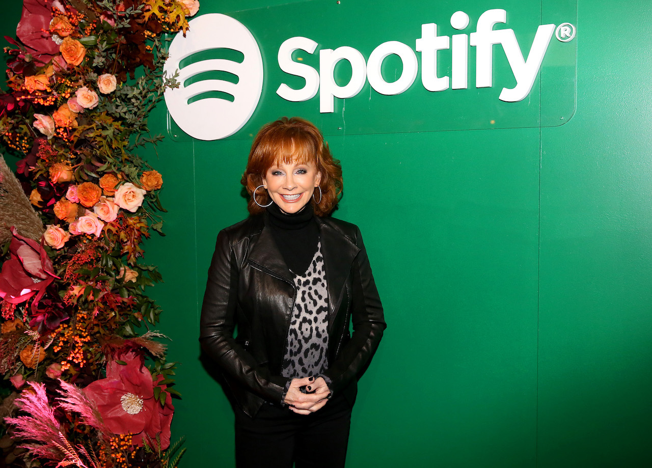 Reba McEntire pose les mains jointes devant elle tout en se tenant devant un fond Spotify