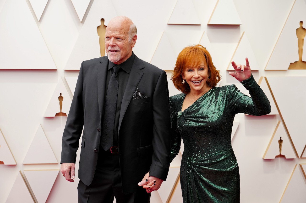 Rex Linn en costume noir, main dans la main avec Reba McEntire en robe vert foncé