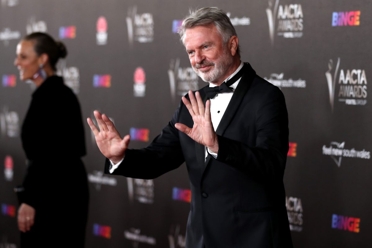 L'acteur Sam Neill portant un smoking levant les mains aux AACTA Awards 2021 devant un step and repeat