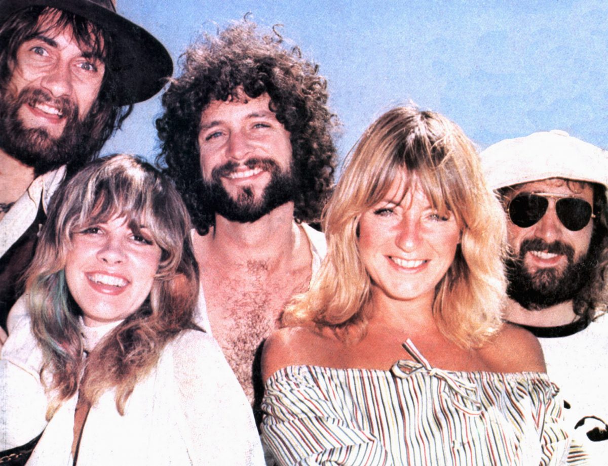 Mick Fleetwood, Stevie Nicks, Lindsey Buckingham, Christine McVie et John McVie sourient sur un fond bleu.