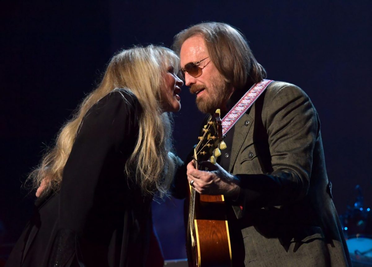 Stevie Nicks parle à l'oreille de Tom Petty.  Il tient une guitare et porte des lunettes de soleil.