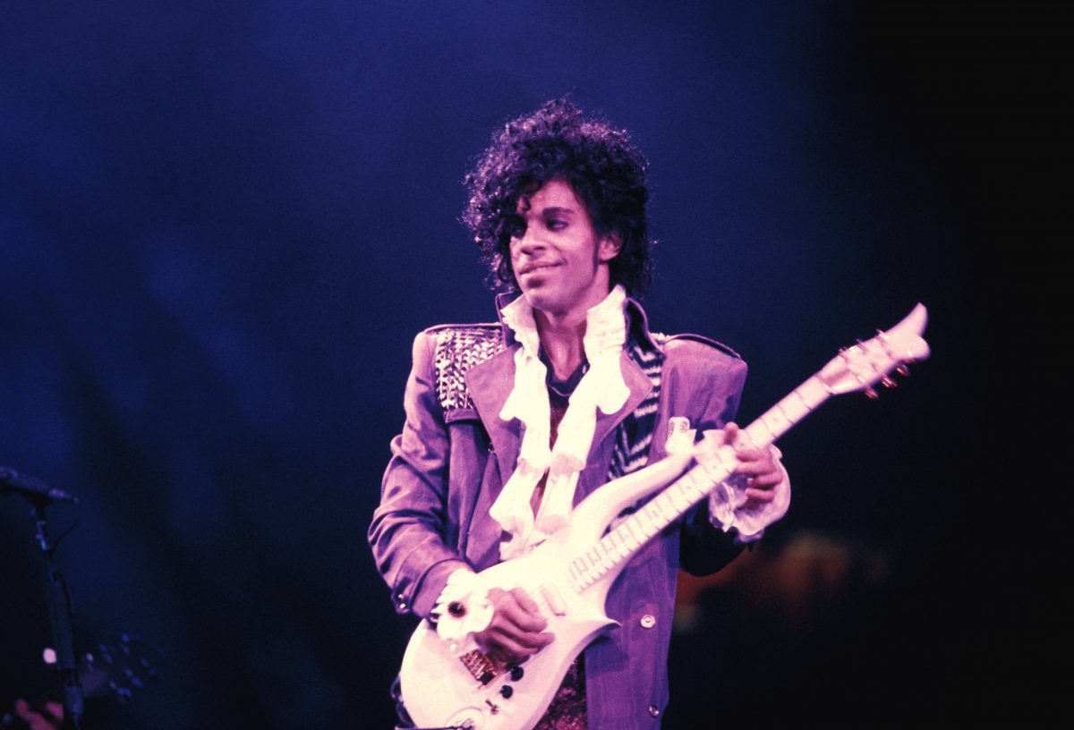 Prince sourit et tient une guitare pendant la tournée Purple Rain. 