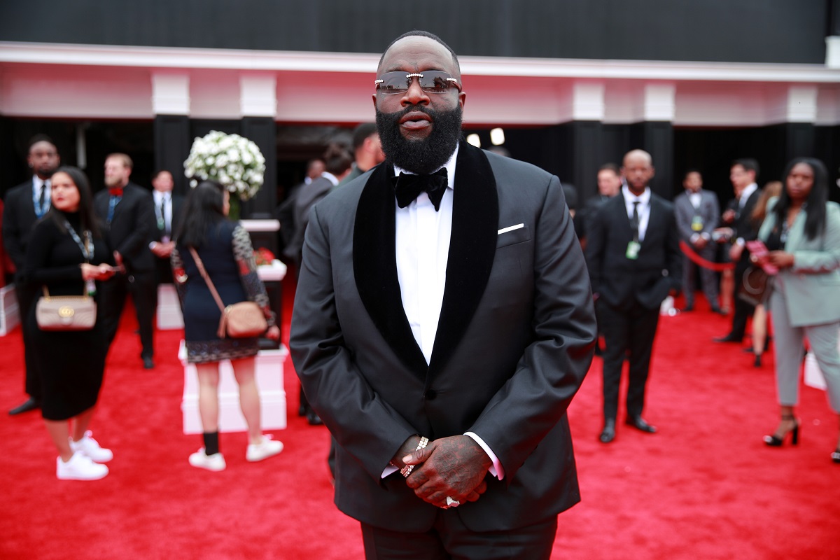 Rick Ross posant tout en portant un costume gris.
