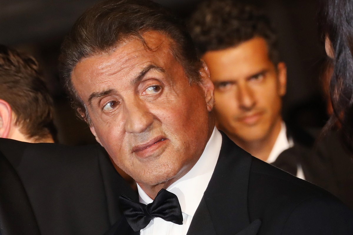 Sylvester Stallone sourit en portant un costume.
