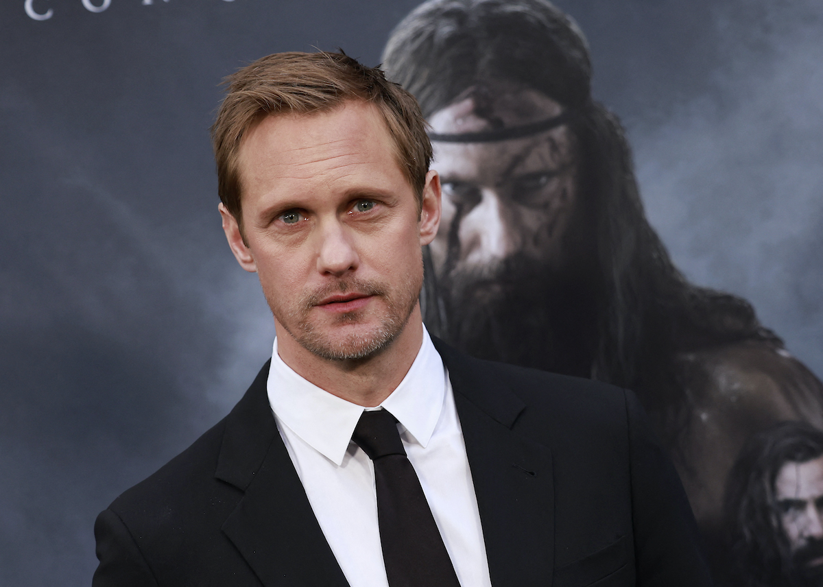 Alexander Skarsgård porte un costume noir et pose devant une image de lui-même dans 'The Northman'