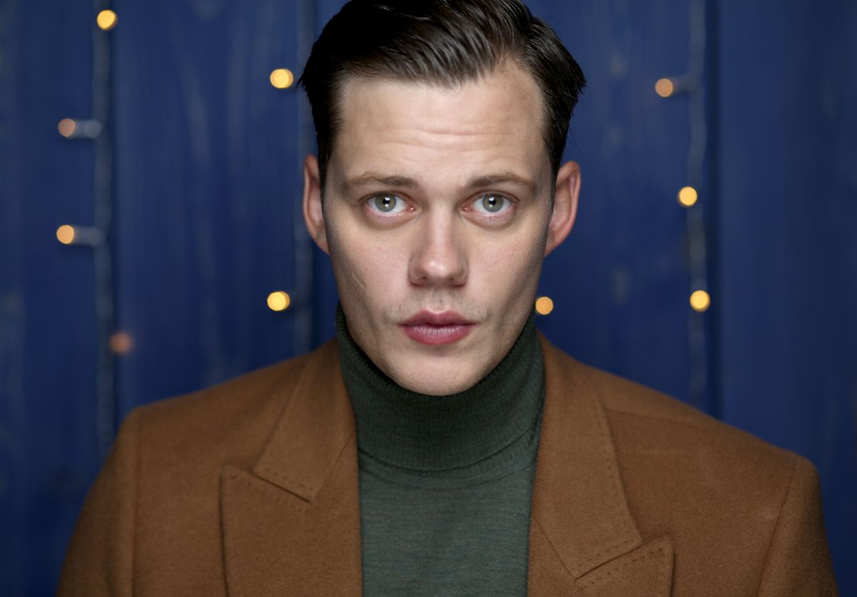 Bill Skarsgård porte une veste marron et regarde directement la caméra.