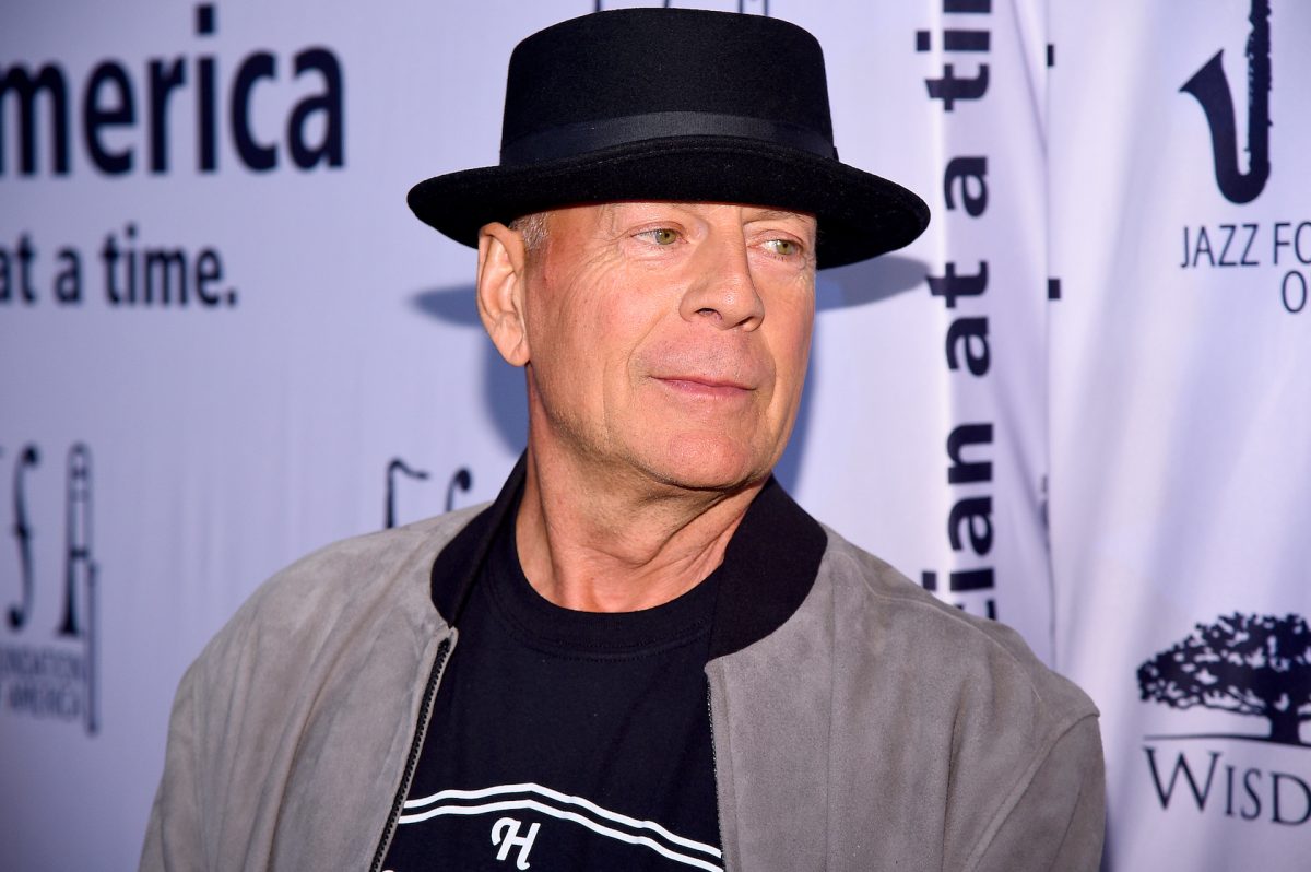 Bruce Willis dans un chapeau noir regardant par-dessus son épaule sur un fond violet.  Bruce Willis quitte Hollywood pour cause d'aphasie
