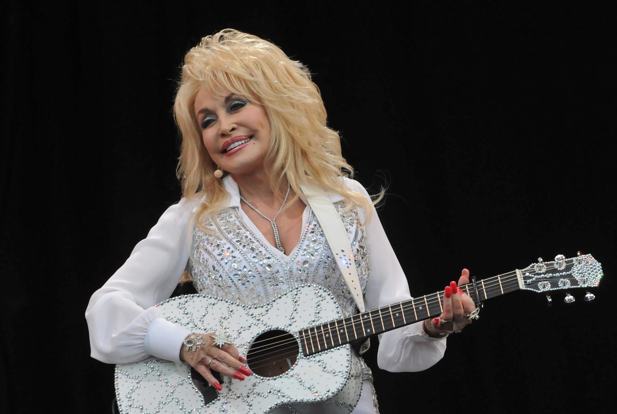 Dolly Parton porte une chemise blanche à strass et tient une guitare assortie.