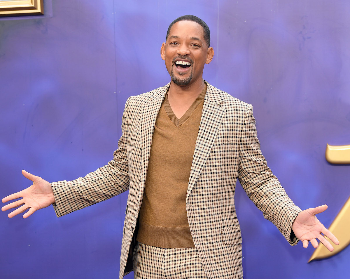 Will Smith sourit avec ses bras devant un fond violet