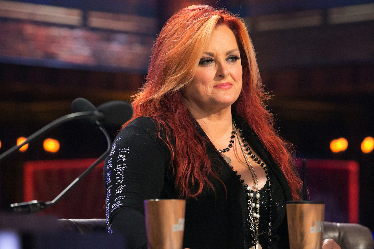 Wynonna Judd en veste noire, assise à une table devant un micro