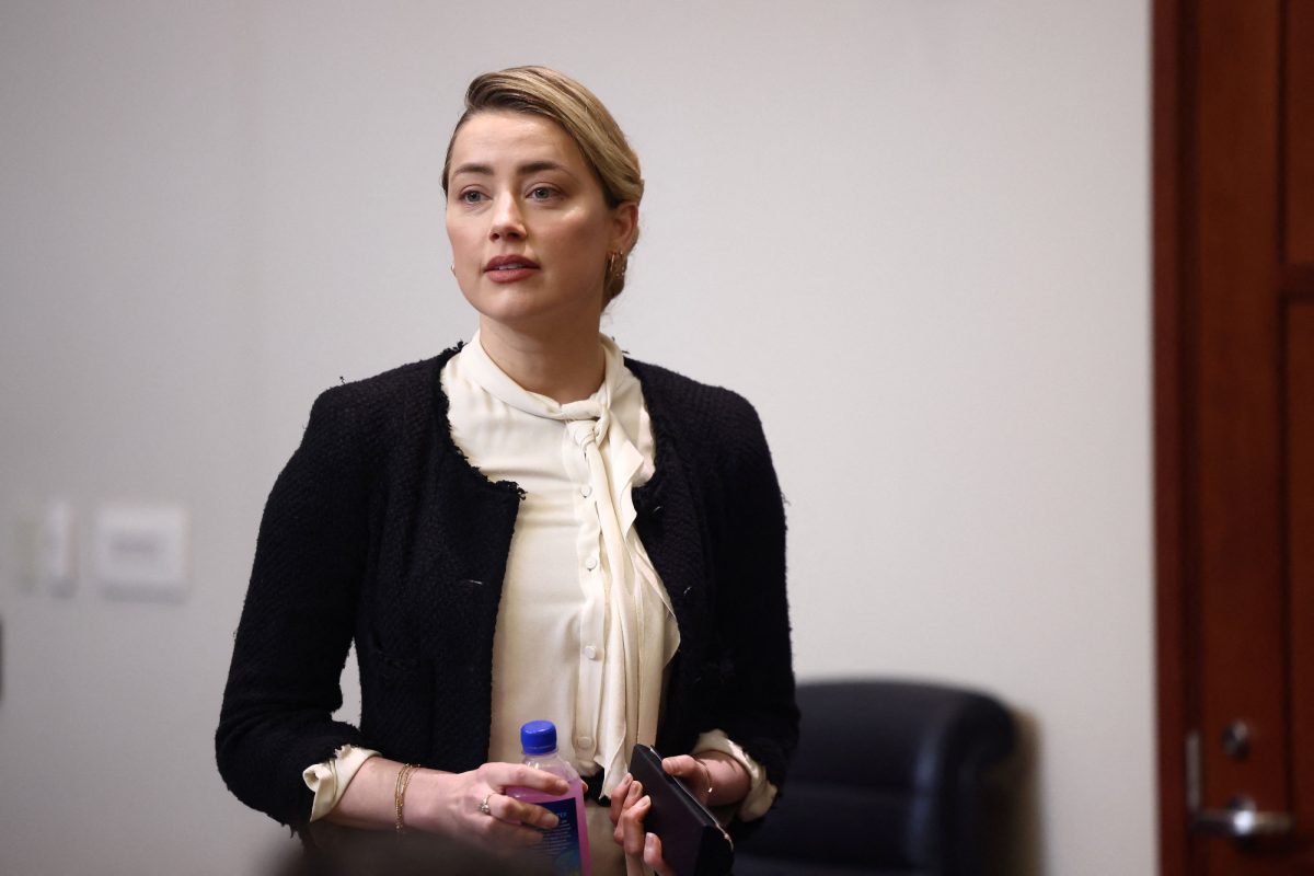 Amber Heard debout tenant une boisson et portant du blanc et du noir