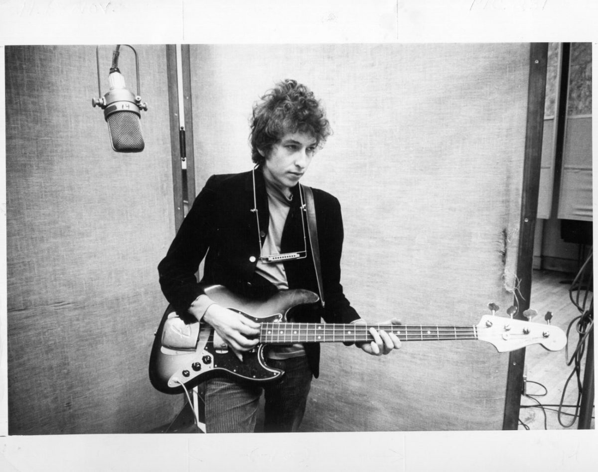 Une photo arrière et blanche de Bob Dylan tenant une guitare dans un studio d'enregistrement.