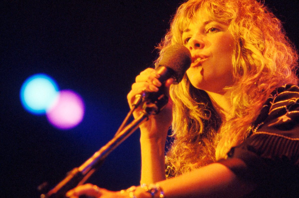 Stevie Nicks porte une chemise rayée et chante dans un micro.