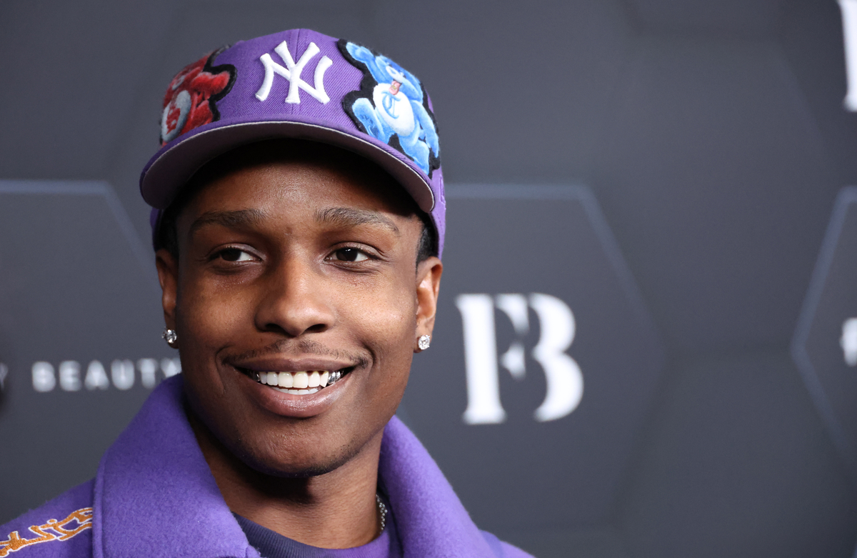 A$AP Rocky porte une veste violette et un chapeau des Yankees tout en souriant lors d'un événement Fenty Beauty.