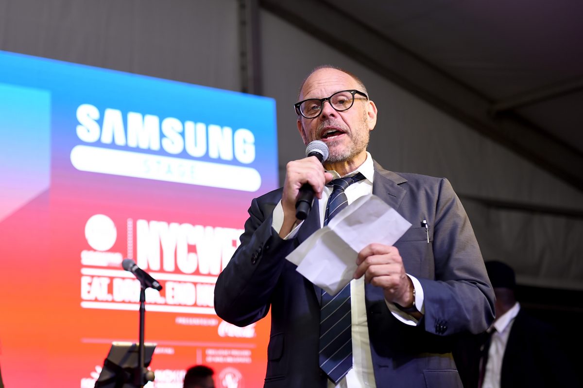 La personnalité culinaire Alton Brown s'adresse à un public avec un microphone à la main.