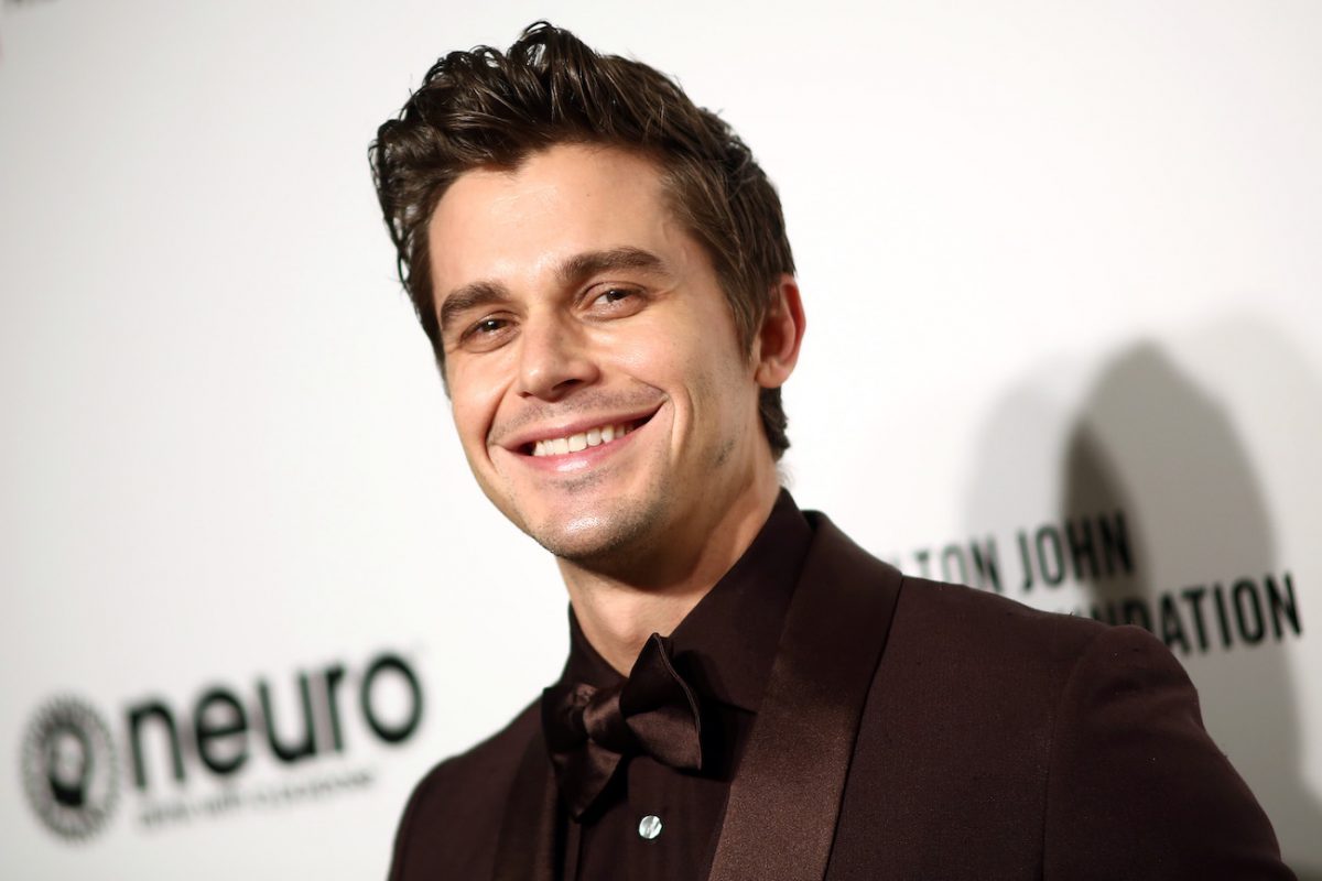 Antoni Porowski portant une tenue grise et souriant devant un fond blanc