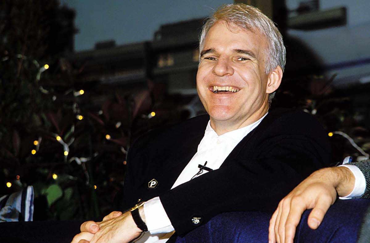Steve Martin porte une veste sombre et rit