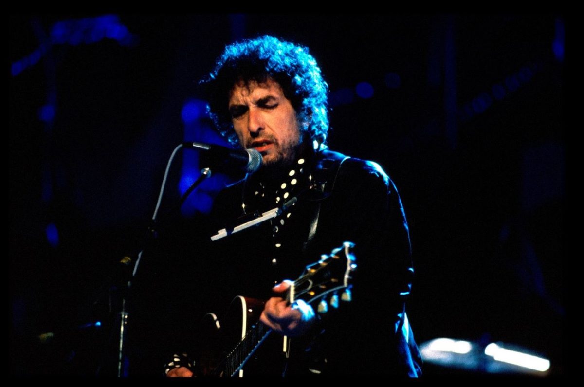 Bob Dylan joue de la guitare et chante dans un micro lors d'un spectacle en 1991.